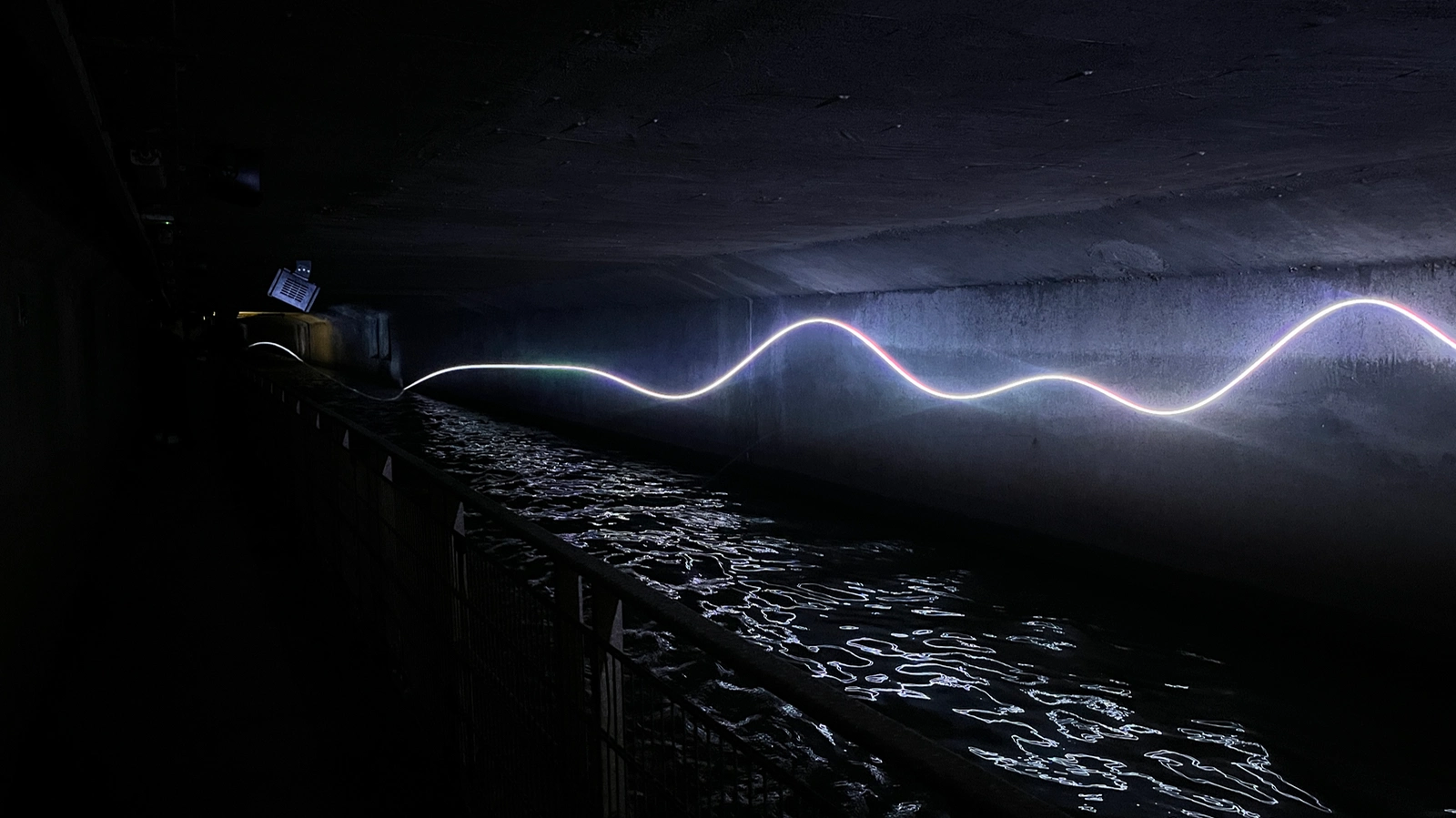 Underground water passage with a glowing line of light along the wall.